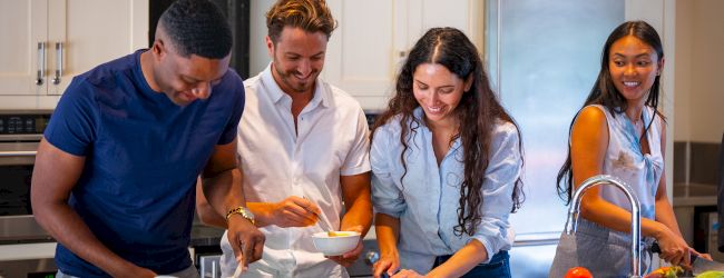 A group of four friends is enjoying themselves while cooking together in a modern kitchen.
