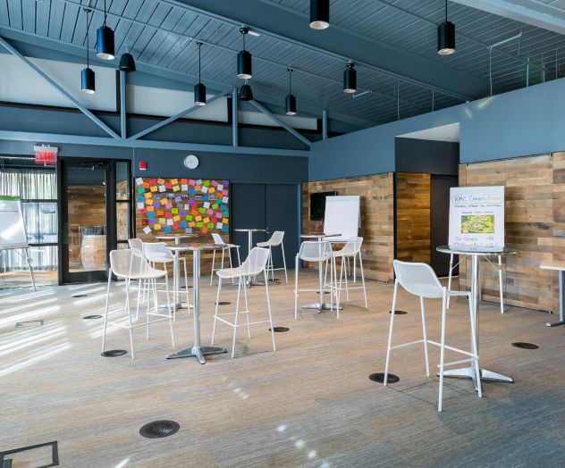 Modern conference room with high ceilings, white bar stools, colorful sticky notes board, flip charts, and a wooden wall.