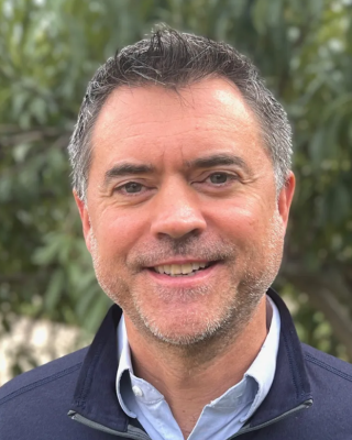 I'm sorry, I don&rsquo;t know who this is. The image shows a person smiling outdoors with trees in the background.